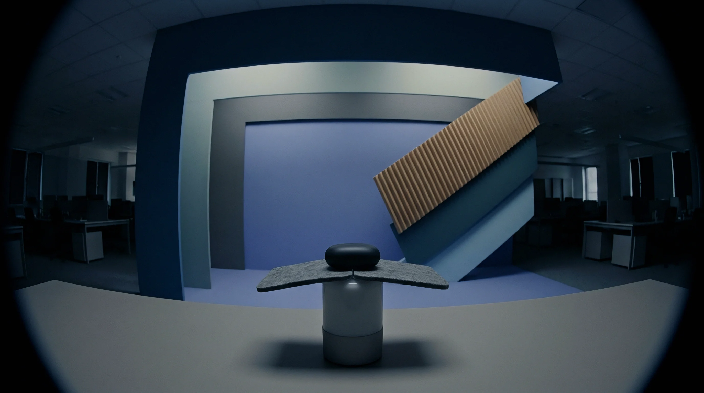 A dark minimalist object rests on an abstract multi-layered platform against a geometric backdrop in a staged facility.