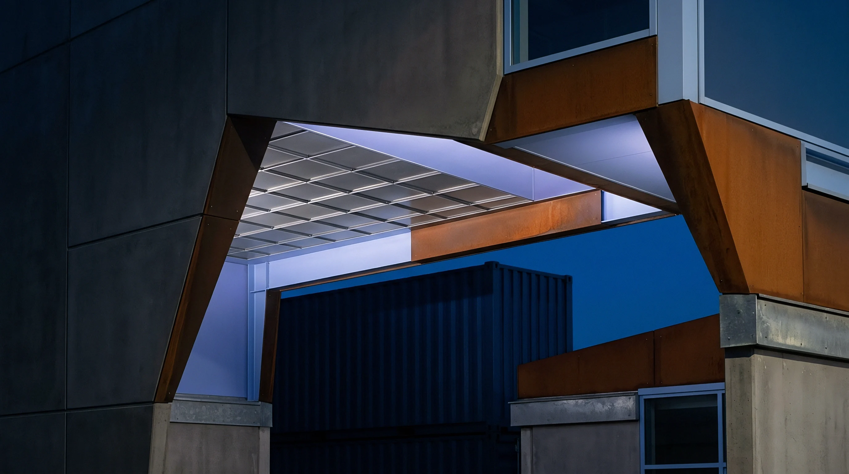 Angular concrete and steel architecture frames a reflection of stacked shipping containers against a deep blue sky.