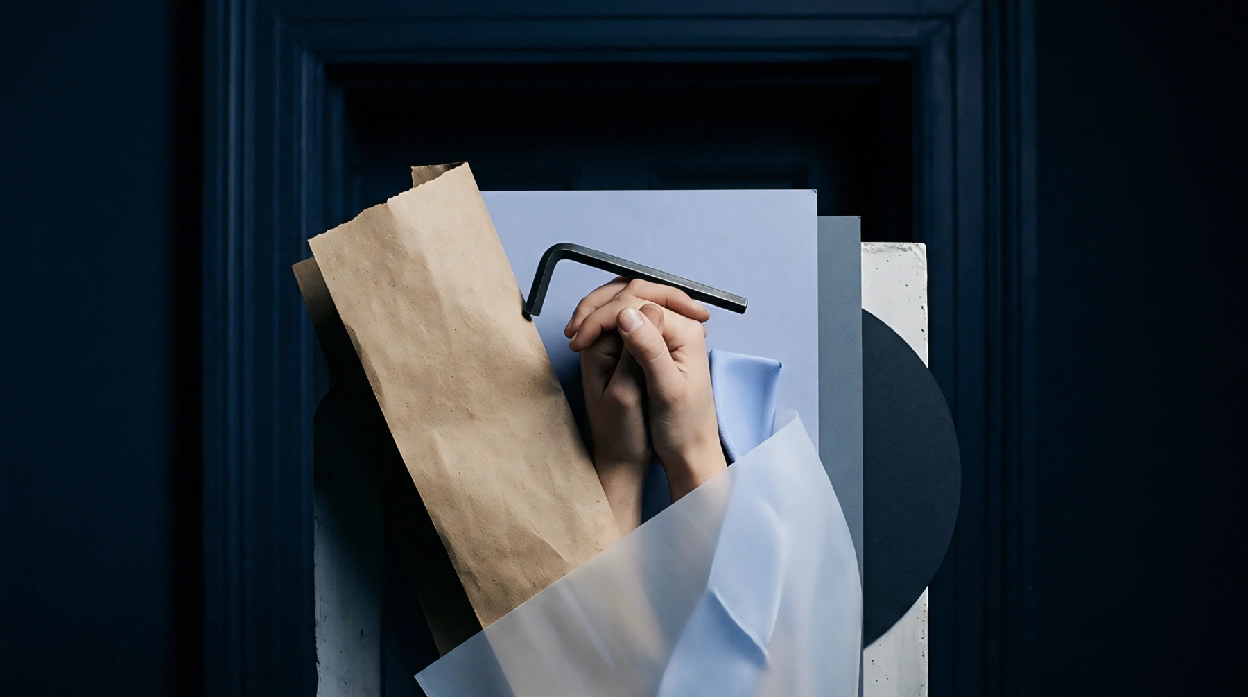 Interlocked hands hold a black hex key above layered sheets of paper and textile samples within a dark doorway frame.