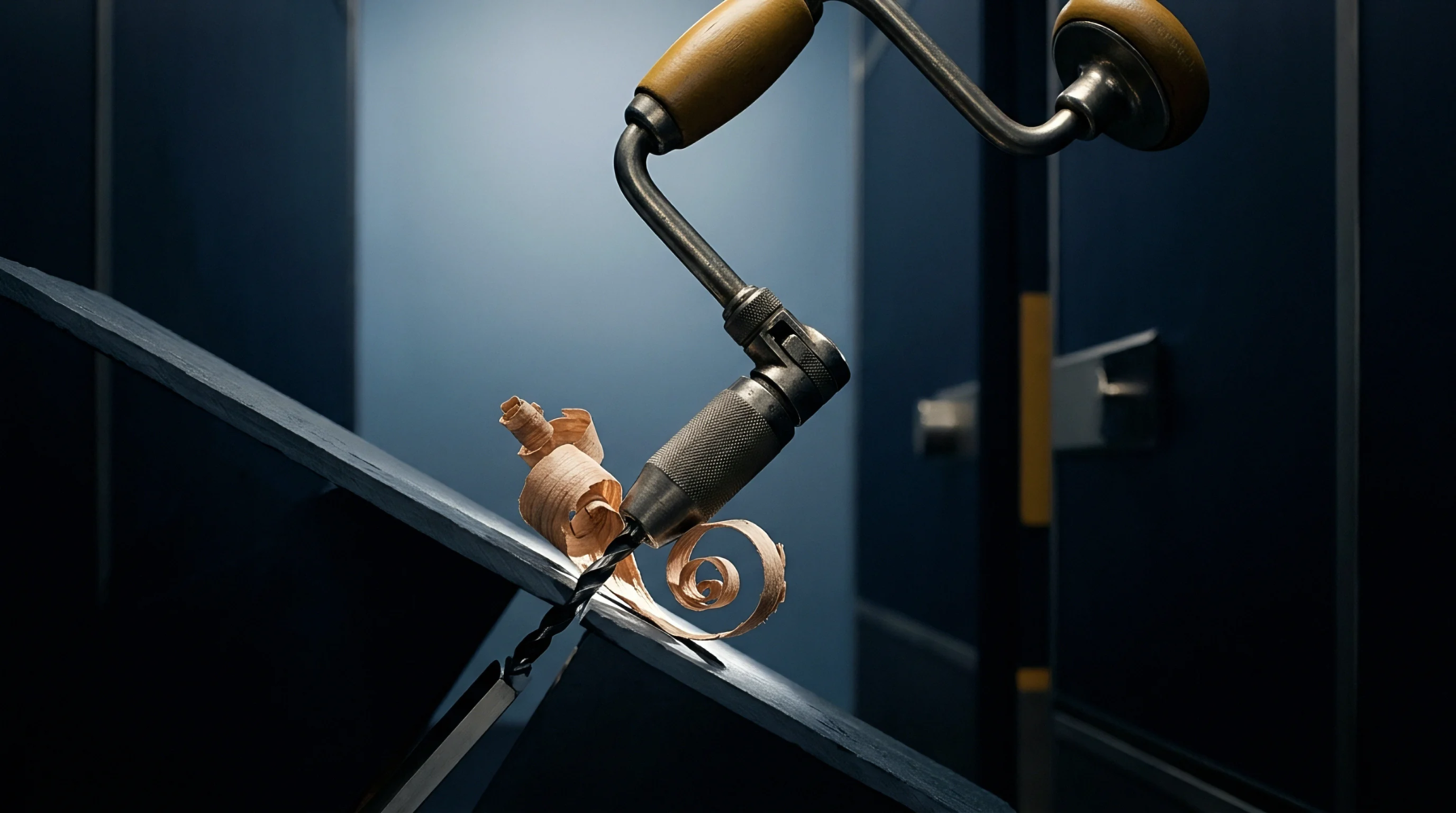 Manual hand brace drill removes material from a dark composite structural component within an organized industrial production environment.