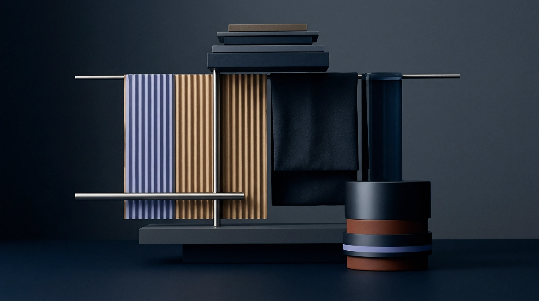 Corrugated metallic sheets and dark fabric samples hang from horizontal metal bars alongside stacked geometric blocks on a neutral dark workspace surface.