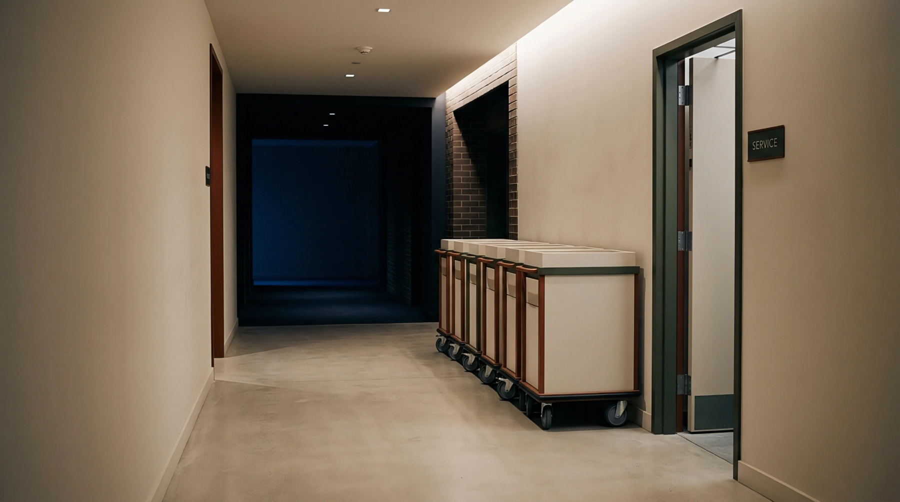 Five identical cream colored modular service carts stand on casters in a well lit industrial corridor near an open service entrance.
