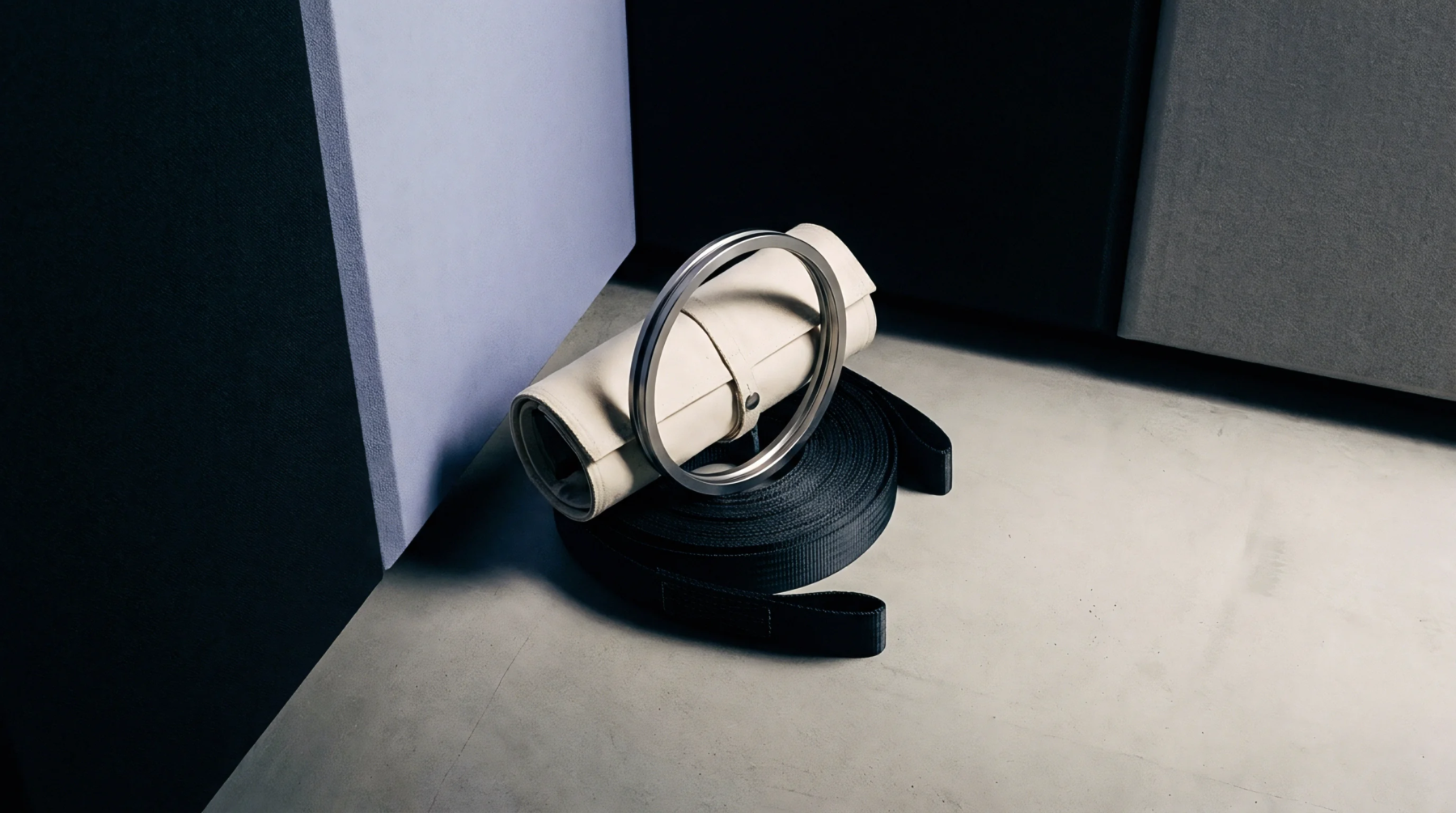 A rolled fabric strap with a steel ring rests on a coiled black nylon webbing band on a concrete floor.