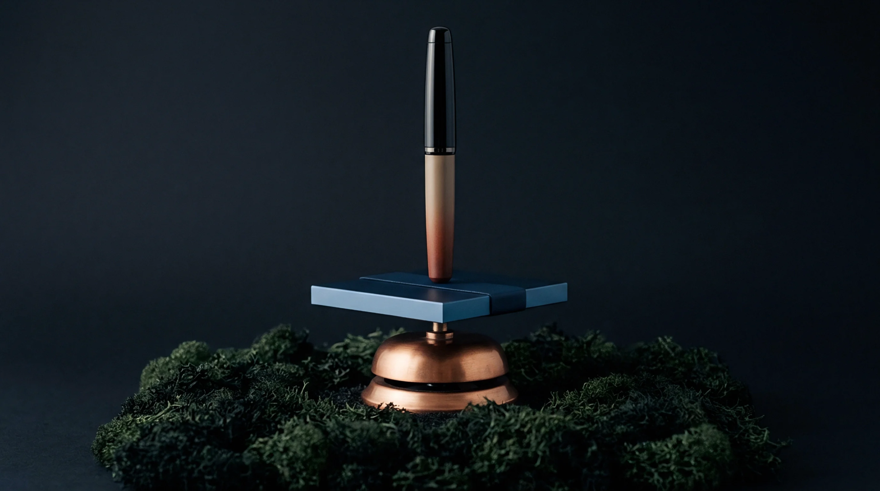 Bronze and black components form a vertical instrument balanced on a blue square platform resting atop a copper call bell within moss.