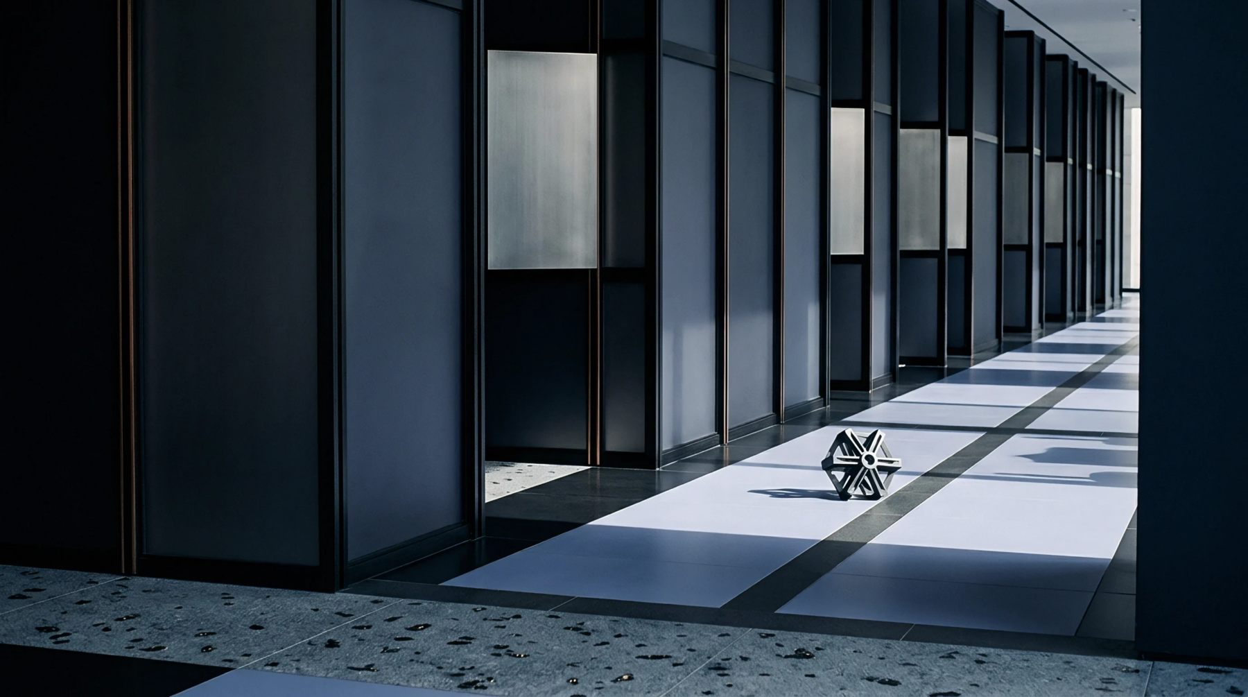 A metallic geometric lattice rests on a tiled industrial corridor floor flanked by dark architectural partition walls inside a manufacturing facility.
